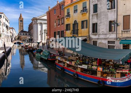 Venedig, Italien - 15. Oktober 2021: Blick auf die Kanäle von Venedig mit Kirche und einem Lebensmittelgeschäft auf einem Boot im Vordergrund Stockfoto