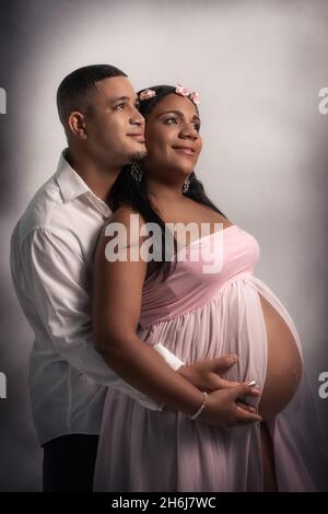 Studioaufnahme eines jungen afroamerikanischen Paares. Die Frau ist schwanger und ihr Bauch ist sichtbar. Sie streicheln beide den Bauch der Frau und haben ein ha Stockfoto