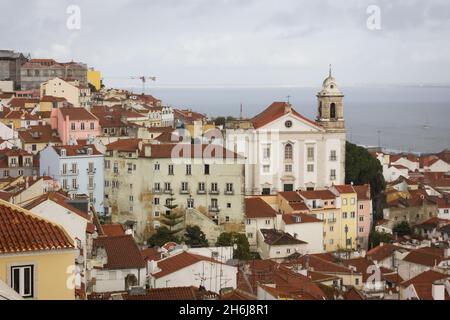 Tolle Aussicht auf Alfama mit Meer im Hintergrund am bewölkten Tag in Lissabon. Farbenfrohe Häuser und Kirche in der portugiesischen Hauptstadt. Traditionelle Altstadt Stockfoto