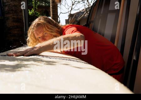 Surfer in rot kämmt das weiße Surfbrett. bali Stockfoto