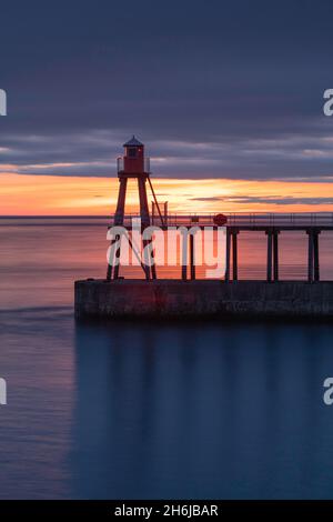 Sonnenaufgang über dem Wasser hinter dem östlichen Pier in Whitby Stockfoto