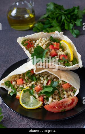 Tabbouleh-Salat mit Bulgur und Petersilie in Pita auf dunklem Teller in Nahaufnahme. Küche des Nahen Ostens Stockfoto