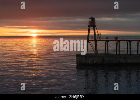 Sonnenaufgang über dem Wasser hinter dem östlichen Pier in Whitby Stockfoto