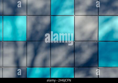 Graue und türkise Quadrate wechseln sich ab. Abstrakte Schatten an der Außenwand des Gebäudes. Das Gebäude ist mit mehrfarbigen Metallblechen verkleidet. Arch Stockfoto