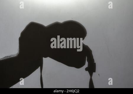 Unschärfe, Unschärfe, Rauschen, Korn-Effekt. Dunkle Silhouette der Hand eines Mannes mit einer spiegellosen Kamera an einer hellgrauen Wand. Mann mit einem modernen fotografischen c Stockfoto