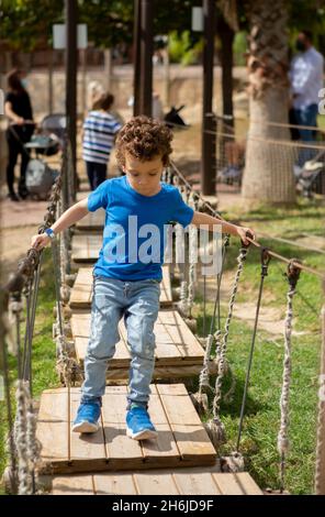 Kleiner Junge, der auf einem Spielplatz eine Holzbrücke überquert Stockfoto