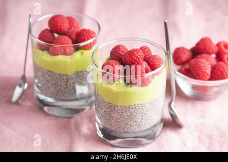 Veganer Chia-Samenpudding mit Avocado-Mousse und Himbeeren im Glas auf rosa Hintergrund Stockfoto