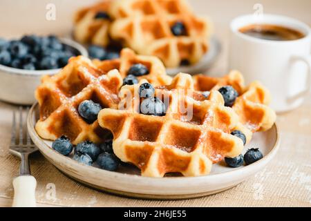 Belgische Waffeln mit Heidelbeeren und einer Tasse Kaffee auf einem Holztisch. Süßes Frühstück Stockfoto