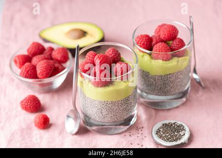Veganer Chia-Samenpudding mit Avocado-Mousse und Himbeeren im Glas auf rosa Textilhintergrund, Nahaufnahme gesundes Dessert Stockfoto