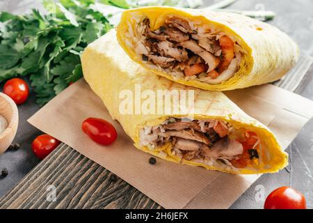 Klassische Shawarma-Rolle mit Huhn und Gemüse in Pita-Brot auf dunklem Holzgrund mit Kirschtomaten und grüner Petersilie Stockfoto