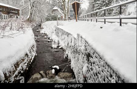 Im Winter fließt ein in Mauern eingezwungener Bach durch verschneite Dörfer im Harz Stockfoto