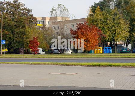 Warschau, Polen - 20. Oktober 2021: Hinter der Stadtstraße befindet sich ein Wohnhaus, in der Nähe gibt es Bäume und auch geparkte Autos Stockfoto