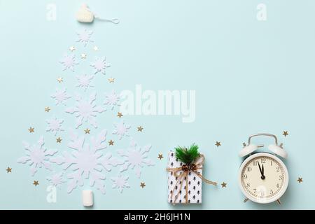 Komposition zu Winterweihnachtszeit. Weihnachtsbaum Form aus Schneeflocken Geschenk Wecker auf blauem Hintergrund. Flach, oben liegend, Kopieplatz Stockfoto