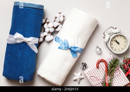 Weiße und blaue Frottee-Handtücher mit Schleife auf hellgrauem Hintergrund. Zweig der Baumwolle Geschenk Wecker Weihnachtsbaum Dekorationen. Stockfoto