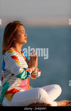 Frau praktiziert Yoga-Meditation am Meer vor Sonnenuntergang als Konzept für Ruhe und Entspannung, Vereinigte Arabische Emirate, Mittlerer Osten Stockfoto