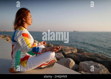 Frau praktiziert Yoga-Meditation am Meer vor Sonnenuntergang als Konzept für Ruhe und Entspannung, Vereinigte Arabische Emirate, Mittlerer Osten Stockfoto