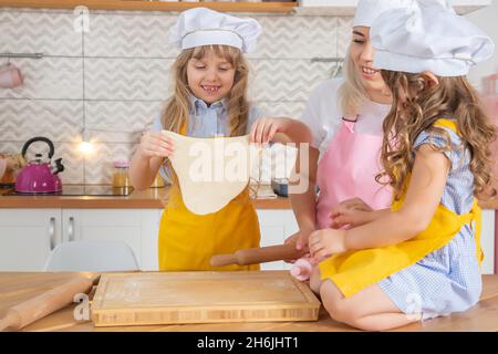 Lächelnde kaukasische Mutter lehrt Töchter, Teig mit Nudelholz in der Küche auszurollen. Hausmannskost-Konzept Stockfoto