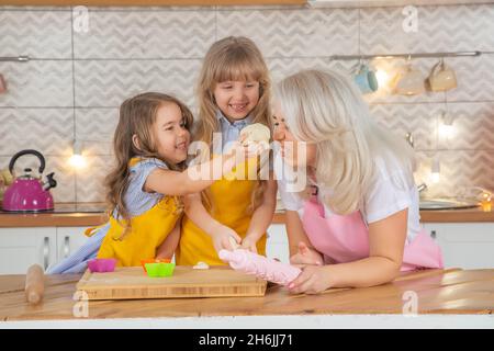 Die 30-jährige kaukasische Mutter hilft ihren süßen kleinen Töchtern beim gemeinsamen Kochen in der Küche. Zwei weibliche Generationen Familie im Kochprozess toget Stockfoto