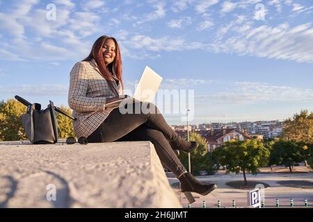 Junge afroamerikanische Frau, die im Freien sitzt und an einem Laptop arbeitet Stockfoto