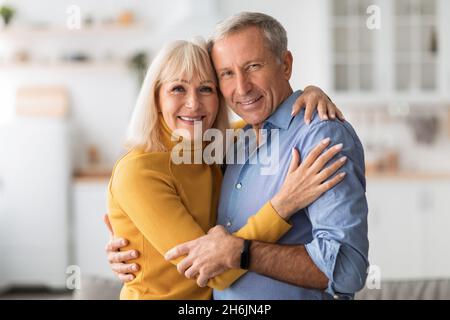 Liebevolles Senior-Paar Umarmt Lächelnd Zur Kamera Zu Hause Stockfoto