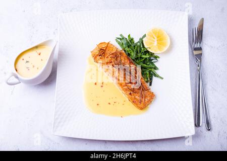 Lachs mit Beurre Blanc Sauce, Spinat und Zitrone. Garniert mit Lauch. Traditionelles französisches Gericht. Nahaufnahme. Stockfoto