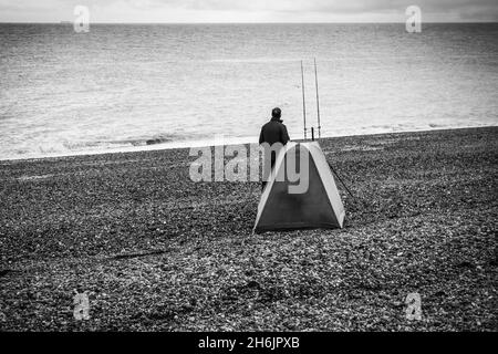 Solitary Fisherman mit seinem Fischerhaus wartet geduldig auf einen Bissen am Strand von Dungeness in einem S&W-Ton, aufgenommen am 14.. November 2021 Stockfoto