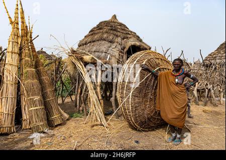 Frau vor ihrer Hütte mit vorbereitetem Schilf, Jiye-Stamm, Staat Eastern Equatoria, Südsudan, Afrika Stockfoto