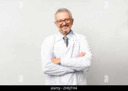 Porträt eines älteren männlichen Arztes auf weißem Hintergrund. Freundlicher Arzt, der lächelt, während er auf die Kamera schaut. Stockfoto