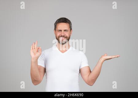 Glücklich Kerl zeigen offene Hand machen OK Ring Geste grauen Hintergrund kopieren Raum, Präsentation Produkt Stockfoto