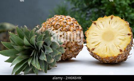 In Scheiben geschnitten und die Hälfte der Ananas (Ananas comosus) auf einem weißen Tisch mit Gartenhintergrund. Stockfoto