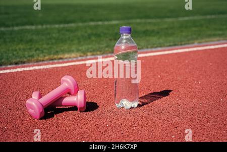 Kurzhanteln auf der Rennstrecke im Stadion. Hydratation nach der Fitness. Gesunde ausgewogene Lebensweise. Pflegen Sie den Wasserhaushalt im Körper während des Trainings. Langhanteln und Stockfoto