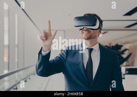 Fröhlicher Geschäftsmann, der bei der Arbeit formell mit einem vr-Headset gekleidet war Stockfoto