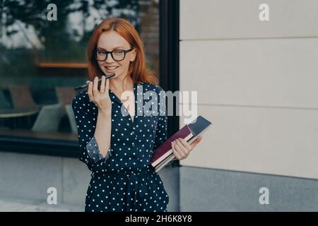 Schöne lächelnde Geschäftsfrau mit Freisprecheinrichtung oder virtuellem Sprachassistenten auf dem Mobiltelefon Stockfoto