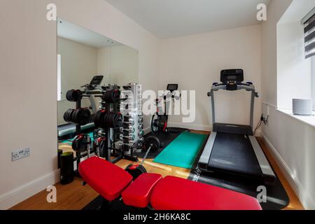 Essex, England - November 18 2019: Indoor häusliche Turnhalle im Haus mit Gewichten, Laufmaschine, Heimtrainer und Bank. Stockfoto