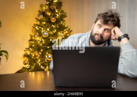 Ein Mann im Büro, müde von der Arbeit und zottelig, sitzt vor einem Laptop und arbeitet Stockfoto