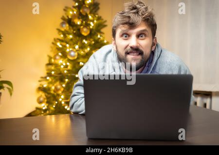 Ein Mann im Büro, müde von der Arbeit und zottelig, sitzt vor einem Laptop und arbeitet Stockfoto