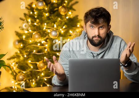 Ein Mann sitzt am Arbeitsplatz, am Silvesterabend im Büro, enttäuscht und schaut hoffnungslos auf die Kamera Stockfoto