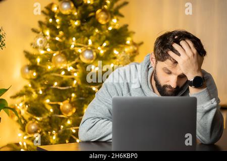 Ein Mann sitzt am Arbeitsplatz, am Silvesterabend im Büro, enttäuscht und schaut hoffnungslos auf die Kamera Stockfoto