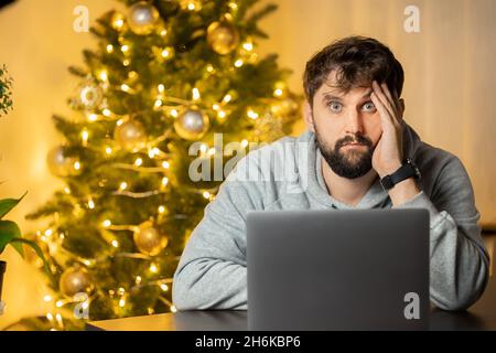 Ein Mann sitzt am Arbeitsplatz, am Silvesterabend im Büro, enttäuscht und schaut hoffnungslos auf die Kamera Stockfoto