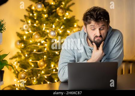 In der Nacht vor weihnachten arbeitet der gequälte Mann am Laptop im Büro Stockfoto