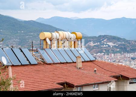 Fässer mit Wasser, die durch Sonnenkollektoren auf dem Dach des Hauses installiert beheizt werden. Konzept der Stromeinsparung. Stockfoto