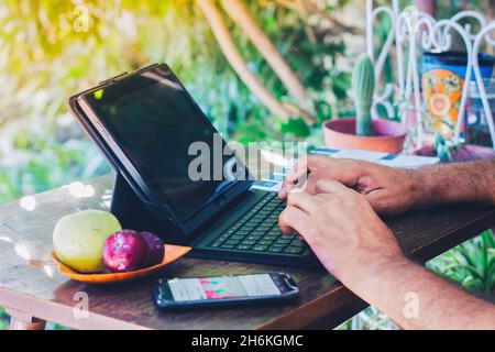 Mann, der sein Notizbuch neben einem frischen Obst und einem Mobiltelefon auf einem Holztisch verwendet - arbeitet von zu Hause aus Stockfoto