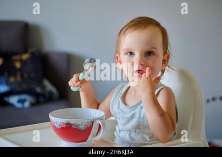 Porträt eines niedlichen kleinen Mädchens, das aus einer Keramikschale Suppe isst und die Kamera anschaut Stockfoto