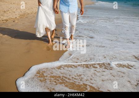 Hochzeitsreise für frisch Vermählte. Barfuß Braut in weißem Kleid und Bräutigam in weißen Hosen zu Fuß auf romantischen Strand. Junge Paar Füße auf goldenem Sand. Stockfoto