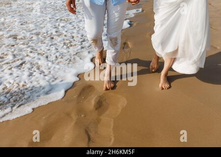 Hochzeitsreise für frisch Vermählte. Barfuß Braut in weißem Kleid und Bräutigam in weißen Hosen zu Fuß auf romantischen Strand. Junge Paar Füße auf goldenem Sand. Stockfoto