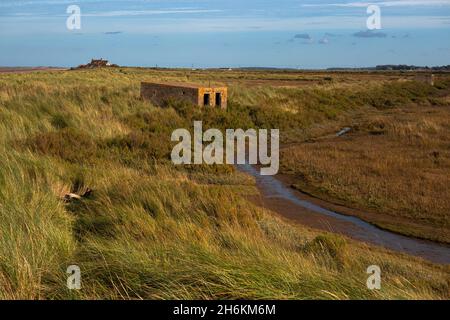 Alte Pillenbox aus dem Zweiten Weltkrieg zwischen den Dünen neben Salzsumpfgebieten am Brancaster Beach im Norden Norfolks in England Stockfoto