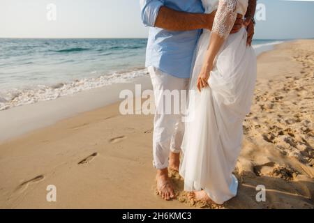 Hochzeitsreise für frisch Vermählte. Barfuß Braut in weißem Kleid und Bräutigam in weißen Hosen zu Fuß auf romantischen Strand. Junge Paar Füße auf goldenem Sand. Stockfoto