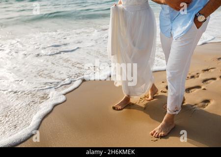 Hochzeitsreise für frisch Vermählte. Barfuß Braut in weißem Kleid und Bräutigam in weißen Hosen zu Fuß auf romantischen Strand. Junge Paar Füße auf goldenem Sand. Stockfoto