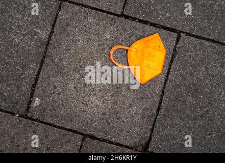 München, Deutschland. November 2021. Ein gebrauchter oranger Mund-Nase-Schutz liegt auf dem Bürgersteig. Kredit: Peter Kneffel/dpa/Alamy Live Nachrichten Stockfoto