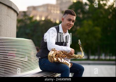 Saxophonist sitzt auf der Bank im Stadtpark Stockfoto